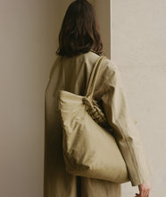 Load image into Gallery viewer, Nylon I Pazar Tote XL Beige plant dyed nylon I beige I from aside I showing the iconic SAGAN closure strap I woman wearing the bag over her shoulder in a gallery