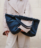 Load image into Gallery viewer, Pazar Tote XL Navy plant dyed nylon mood picture I French lady is wearing the bag casually with one hand under her arms leaning against a wall in Paris I Zoomed in picture with focus on the bag.