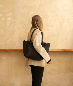 Nylon I Pazar Tote M I charcoal black plant dyed japanese nylon I front view I showing the iconic SAGAN closure strap I model wearing the bag over her shoulder at SAGAN Vienna Shop